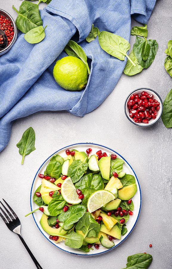 Vegan Salad With Pineapple, Spinach, Avocado And Pomegranate, Gr Vegan salad with pineapple, spinach, avocado and pomegranate, gray table, top view. Healthy eating, clean food, diet, weight loss concept