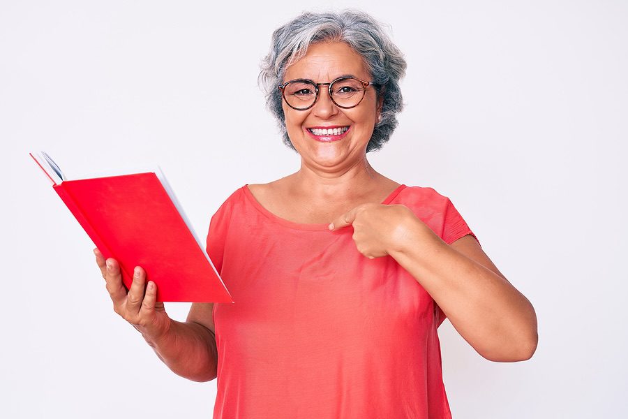 Senior hispanic woman wearing glasses holding book pointing finger to one self smiling happy and pro woman senior
