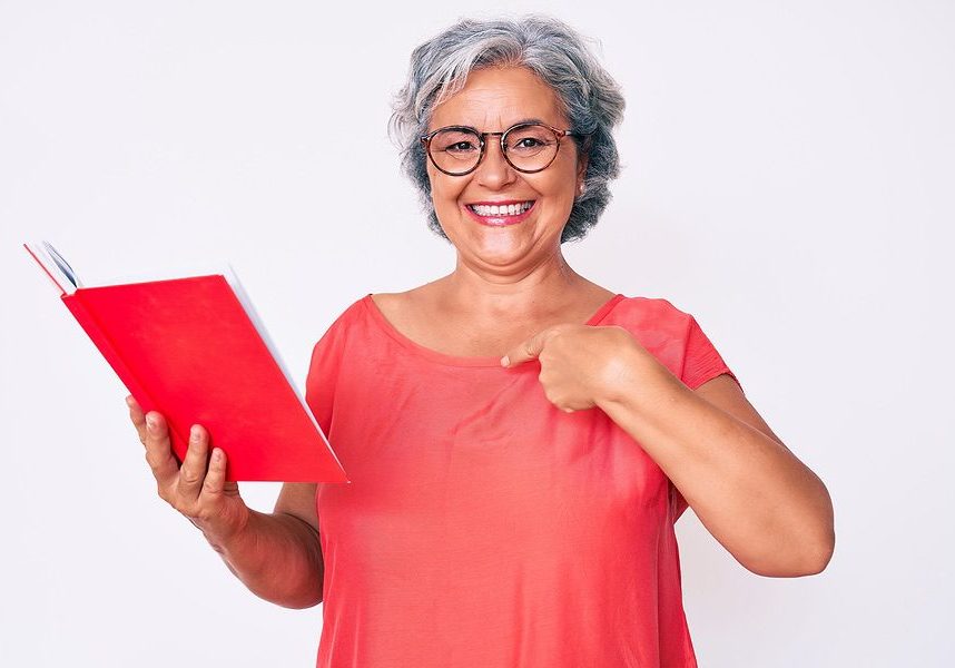 Senior hispanic woman wearing glasses holding book pointing finger to one self smiling happy and pro woman senior