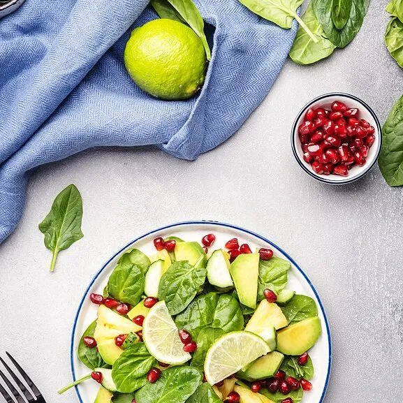 Vegan salad with pineapple, spinach, avocado and pomegranate, gray table, top view. Healthy eating, clean food, diet, weight loss concept